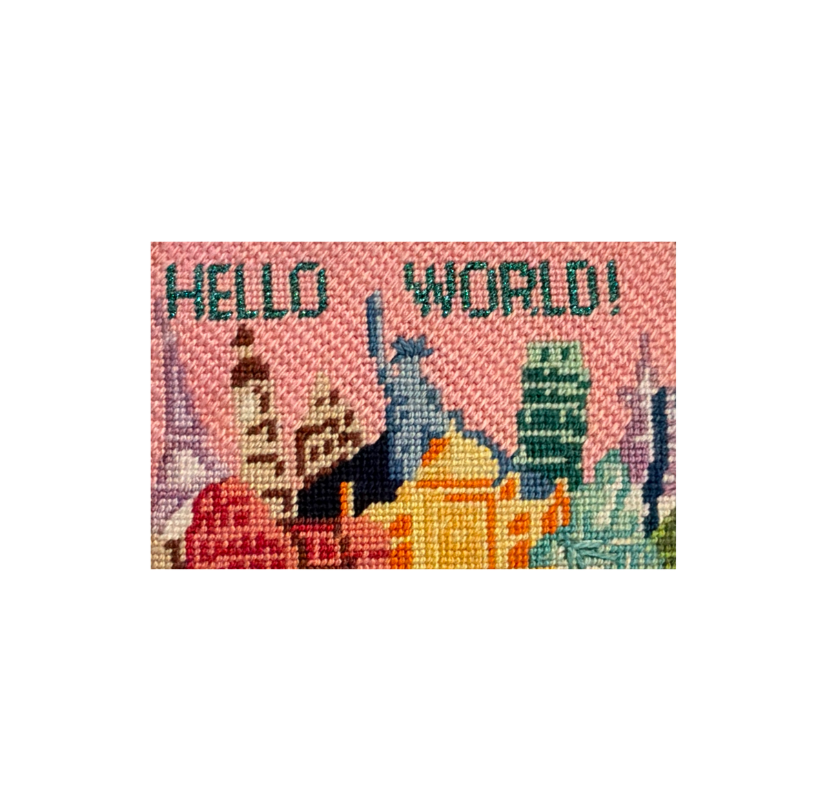 Needlepoint canvas stitched with a pink city skyline reading HELLO WORLD, ready to be finished into FFF leather goods.